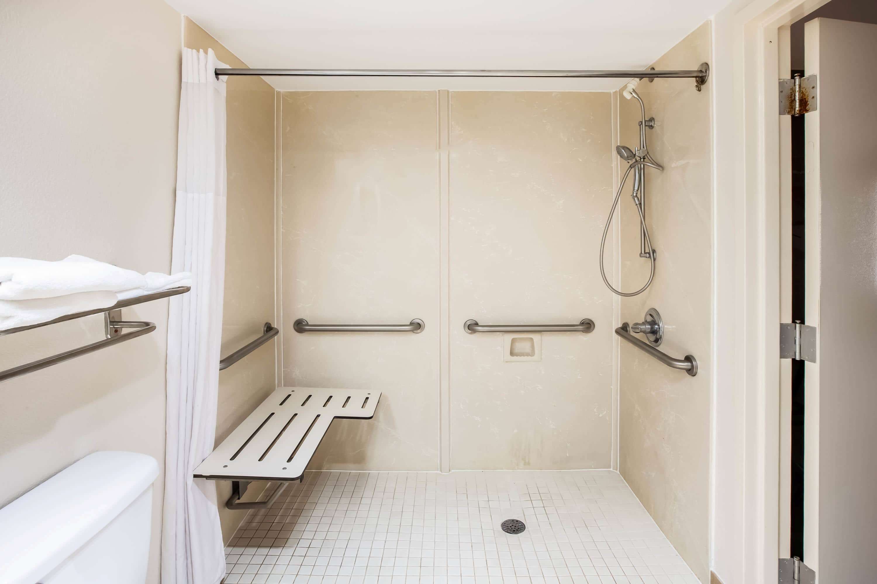 A wheelchair-accessible shower area with grab bars, a bench, and a toilet.