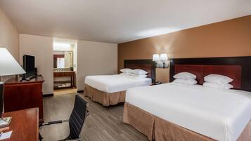 A hotel room with two beds, a desk, a chair, a television, and a bathroom visible in the background.