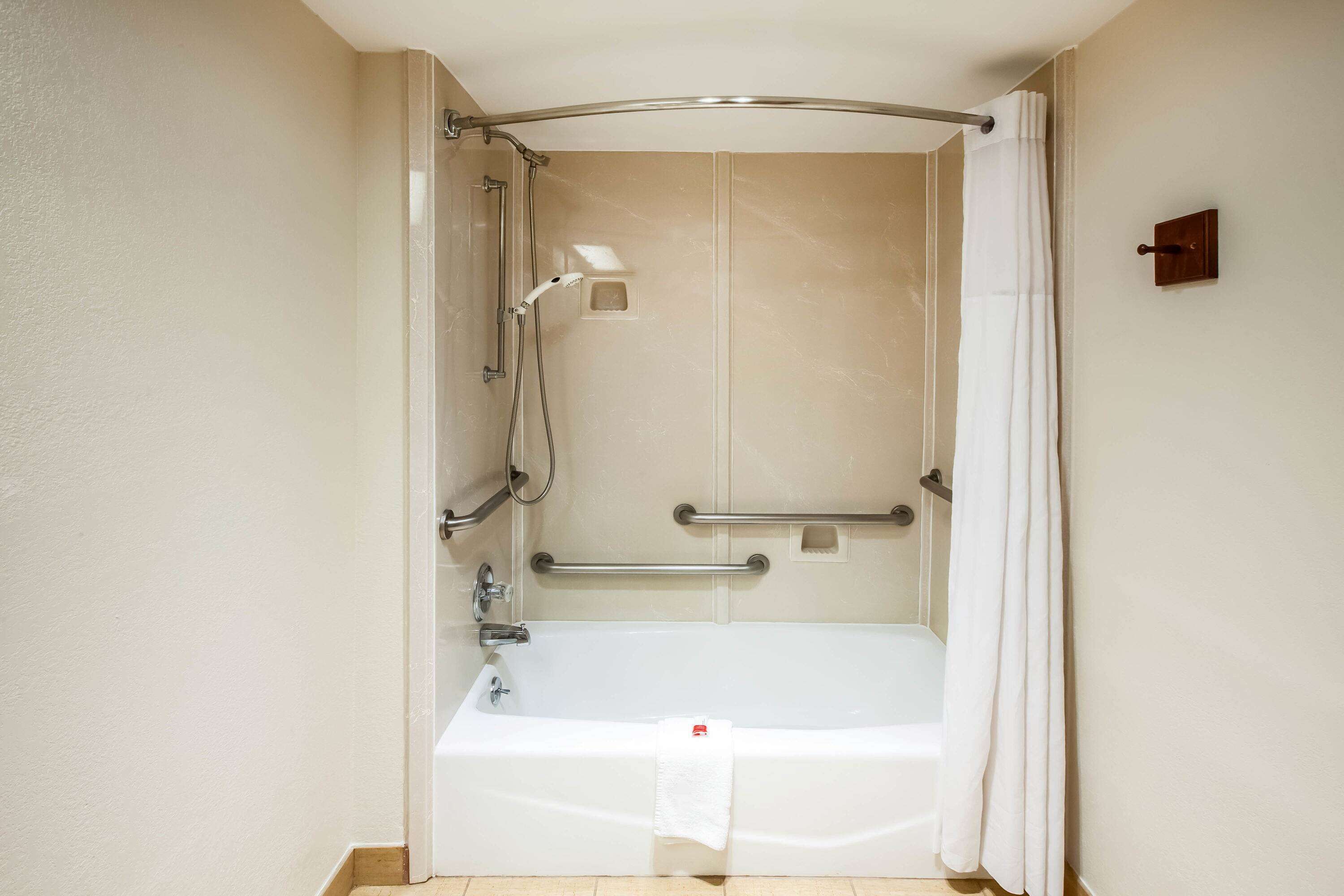 Ducha a pie con bañera, barras de apoyo y cabezal de ducha.