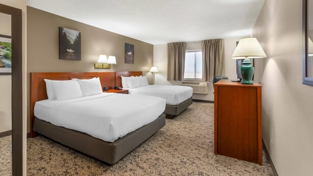 A hotel room with two beds, a wooden headboard, a desk with a lamp, and a window with curtains. - Quality Inn & Suites Fillmore I-15 (Fillmore)