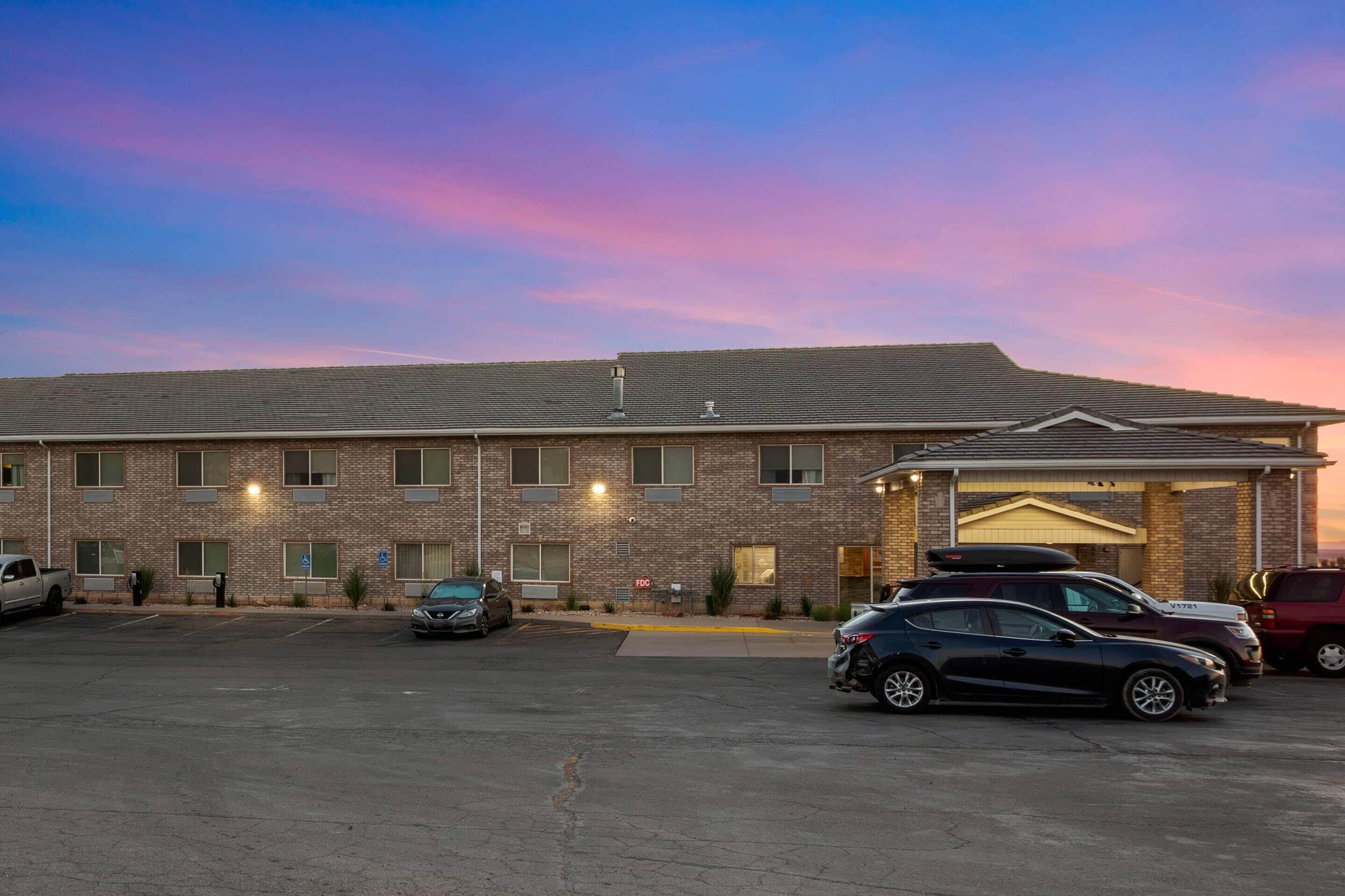 A multi-story hotel with a brick facade, a covered entrance, and a parking lot with several cars.