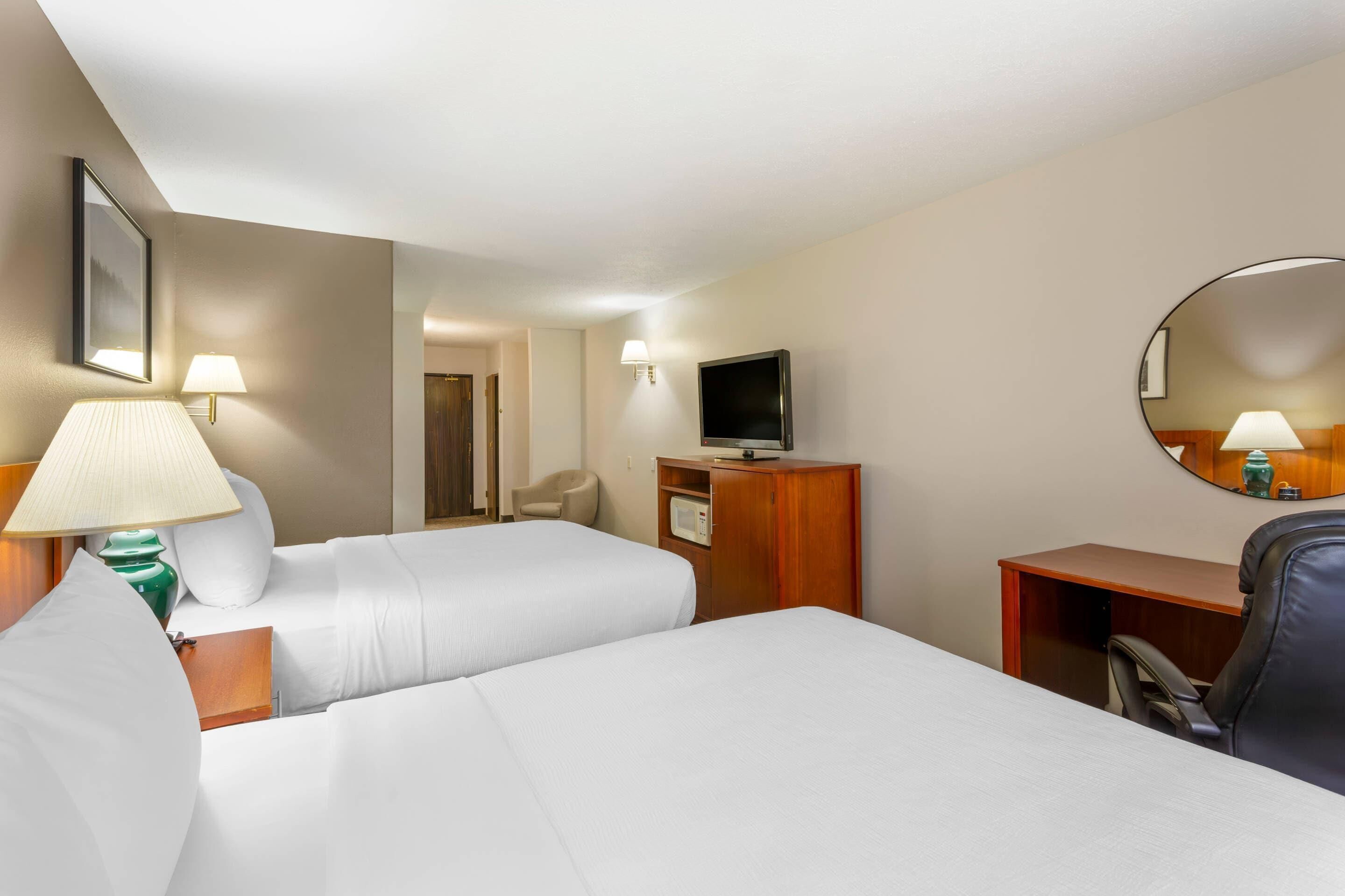 A hotel room with two beds, a desk, a chair, a TV, and a mirror.