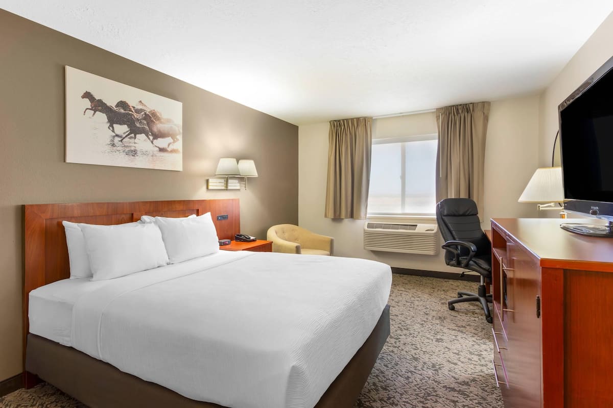 A hotel room with a large bed, a desk with a computer, a chair, a TV, a window with curtains, and a painting on the wall.