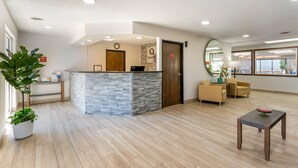 A reception area with a stone counter, wooden door, and a clock on the wall. There are potted plants, a small table, and a sofa in the room. - Quality Inn & Suites Fillmore I-15 (Fillmore)