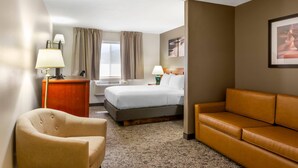 A hotel room with a bed, a desk, a chair, a sofa, and a window with curtains. - Quality Inn & Suites Fillmore I-15 (Fillmore)