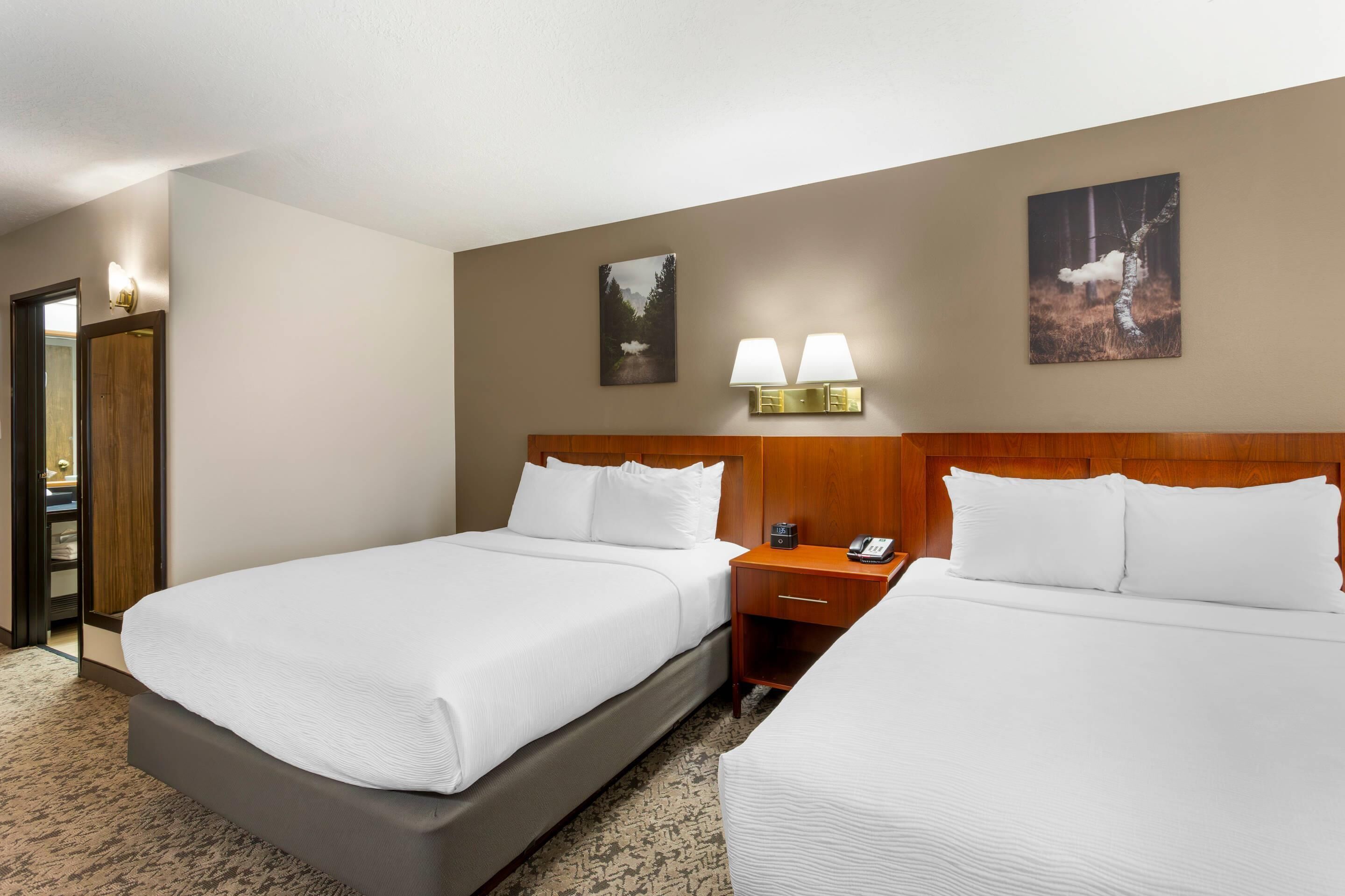 A hotel room with two beds, a wooden headboard, bedside tables with lamps, and artwork on the walls.