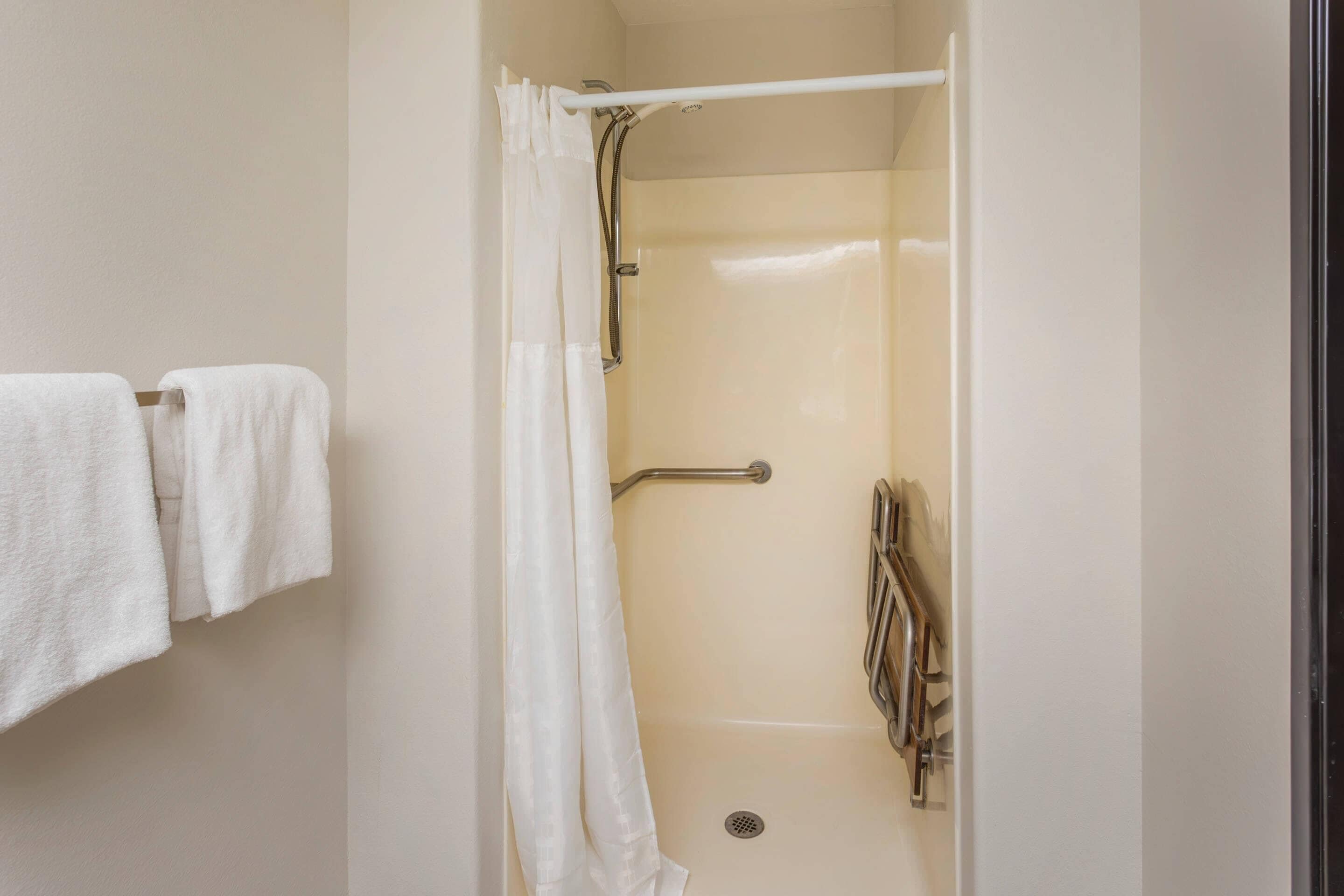 A shower with a white curtain, a grab bar, and a towel rack with two towels.