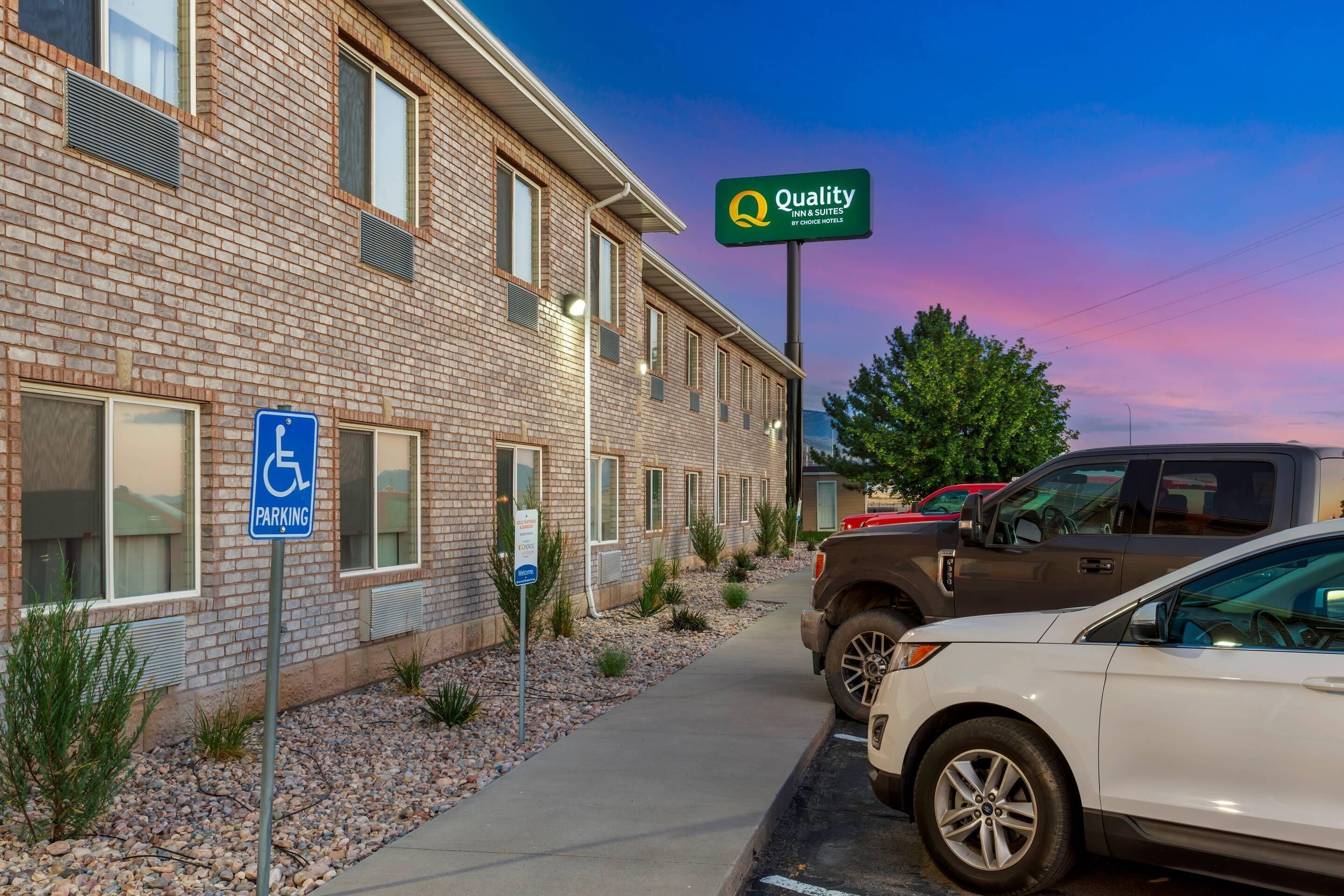 A hotel with a brick facade, a handicap parking sign, and a sign indicating it is a Quality Inn & Suites by Choice Hotels.