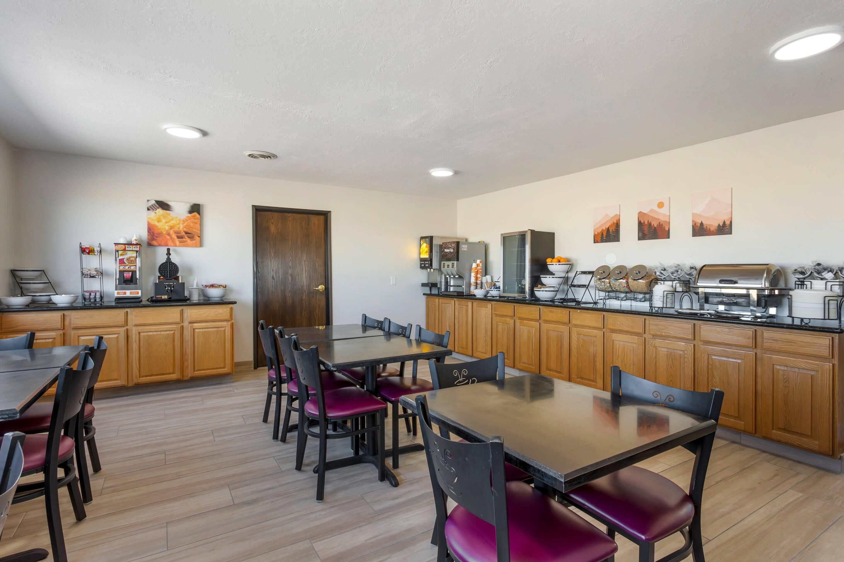 A modern kitchen with wooden cabinets, a dining area with red chairs, and a coffee station.