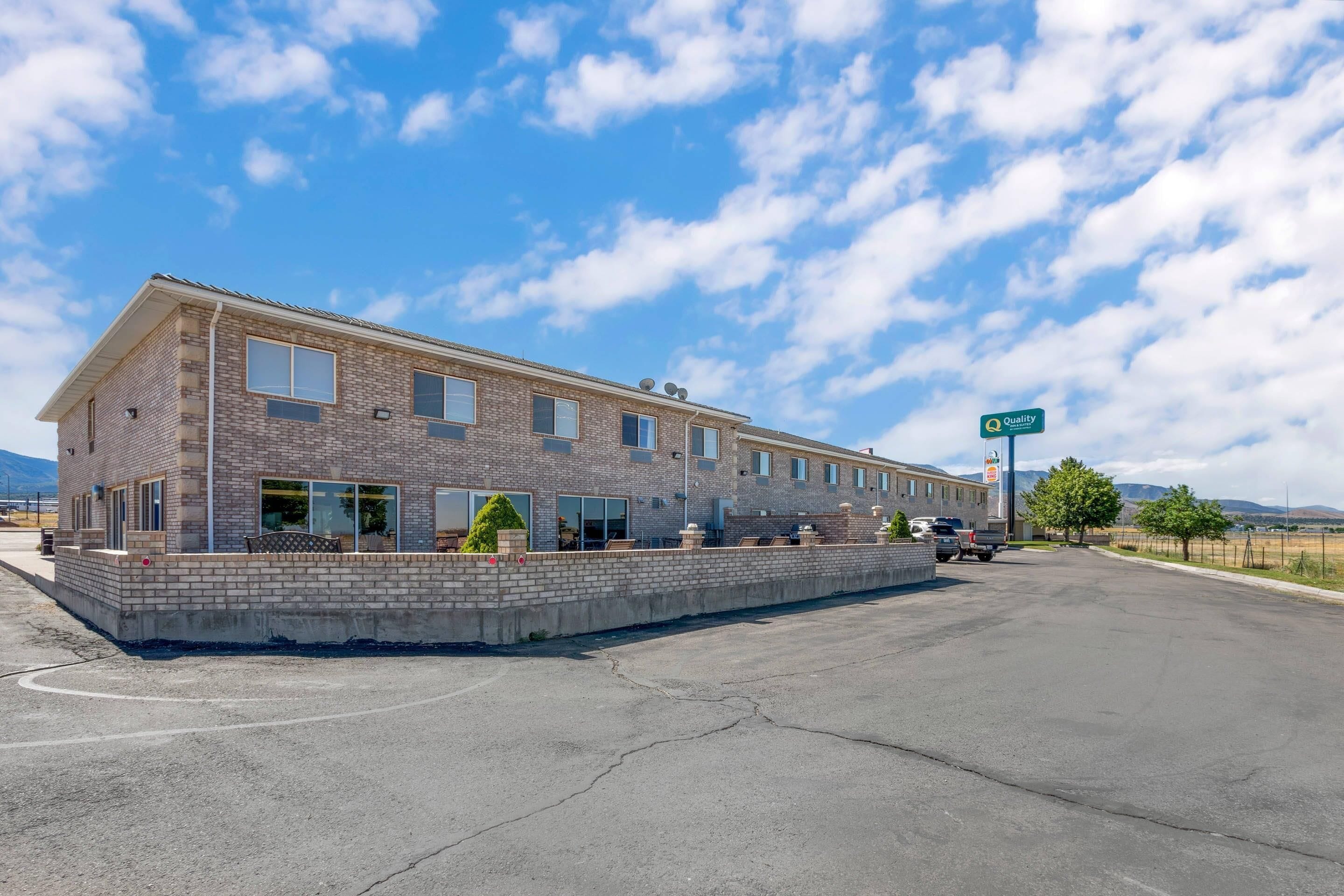 A two-story brick building with a flat roof, large windows, and a parking lot in front.