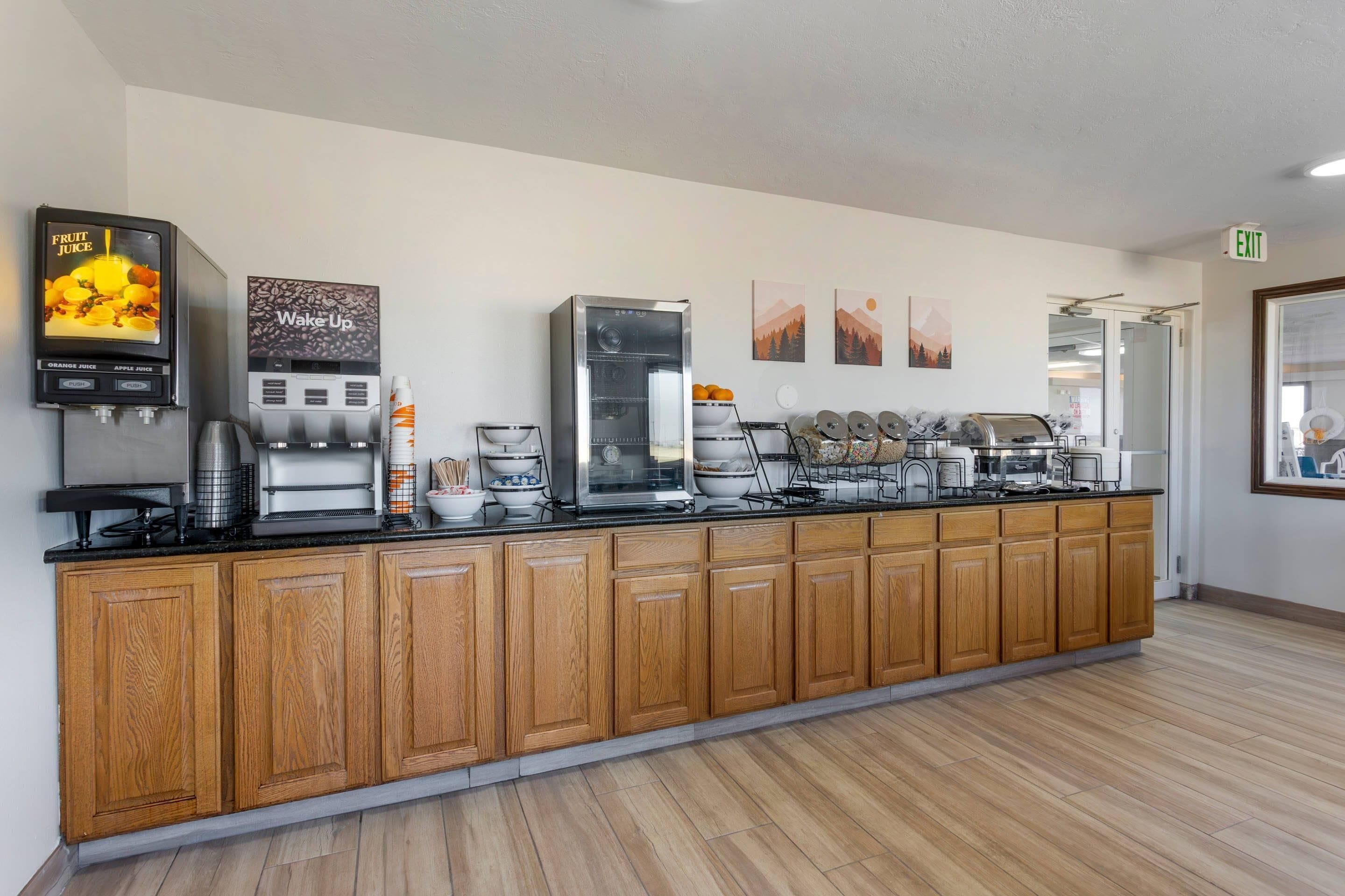 A long wooden counter with a coffee machine, a fruit juice dispenser, and a "Wake Up" coffee station.