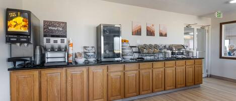 A long wooden counter with a coffee machine, a fruit juice dispenser, and a "Wake Up" coffee station.