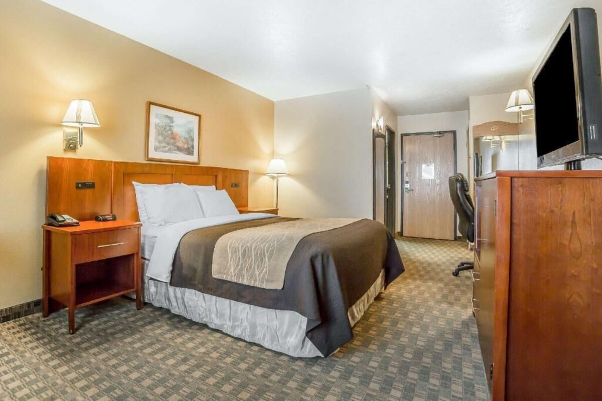 Ein Hotelzimmer mit Bett, Nachttisch, Lampe, Fernseher und Schreibtisch mit Stuhl.
