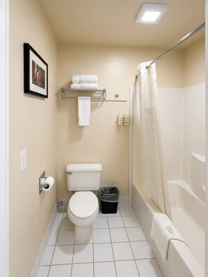 A small bathroom with a toilet, a shower with a curtain, a towel rack, and a picture on the wall. - Ramada by Wyndham Draper (Draper)