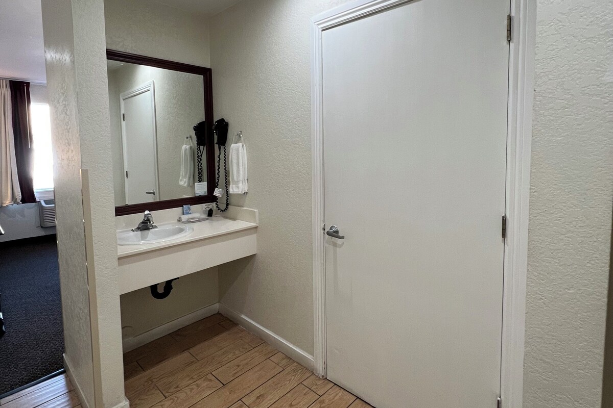 A bathroom with a white sink, mirror, and door, wooden flooring, and a ceiling light.