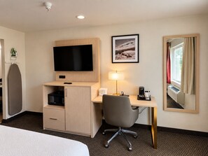 Habitación de hotel con una cama, un escritorio con silla, televisión, cafetera y un cuadro en la pared.