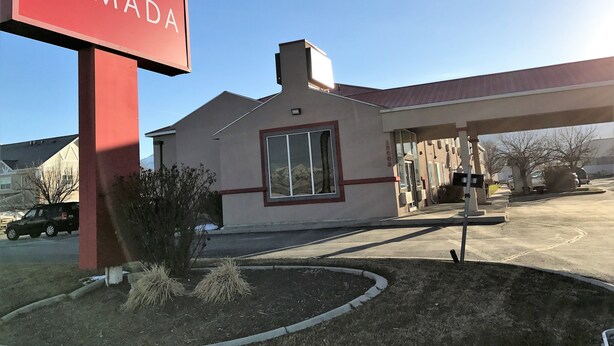 Un edificio con un letrero 'RAMADA', una estación de servicio y un estacionamiento con vehículos.