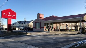 Una estación de servicio con un letrero rojo que dice "RAMADA" y un edificio de fachada color crema con detalles rojos.