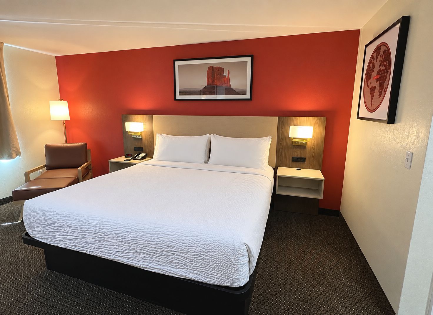 Una habitación de hotel con una cama grande, dos mesitas de noche con lámparas, una silla e imagen enmarcada en la pared.