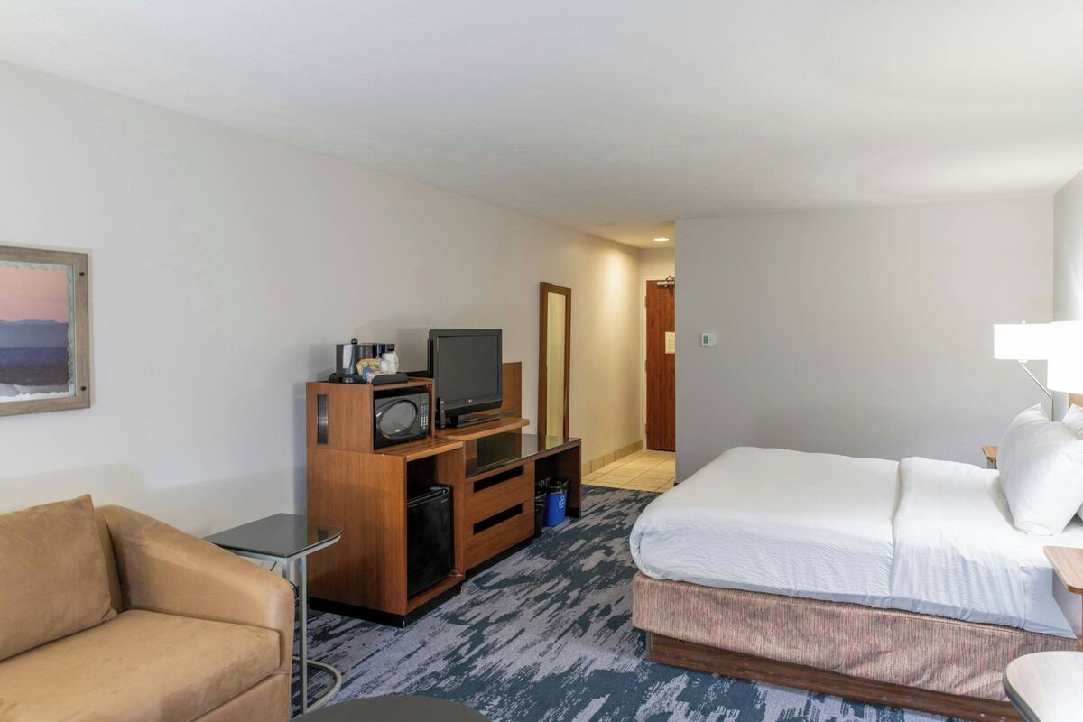 A hotel room with a bed, a sofa, a TV, and a wooden cabinet.