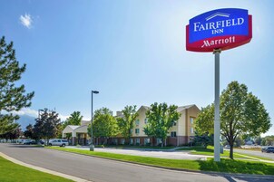 A Fairfield Inn Marriott sign, a multi-story building with a beige facade, and a parking lot with several cars.