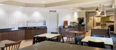 Una cocina moderna con estufa integrada, cafetera y refrigerador. Hay varias mesas y sillas de madera, y una isla grande con pileta.