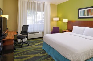 Una habitación de hotel con una cama, un escritorio con una computadora, una silla, una lámpara y un cuadro en la pared.