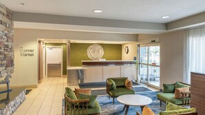 A hotel lobby with a reception desk, seating area with green upholstered chairs, a coffee table, and a view of the outside through large windows. - Fairfield Inn by Marriott Salt Lake City Layton (Layton)