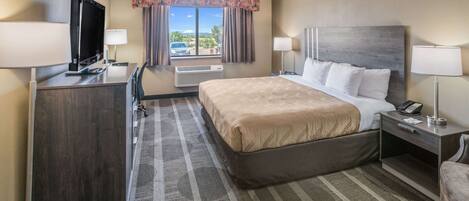 A hotel room with a bed, desk, TV, and a window with curtains.