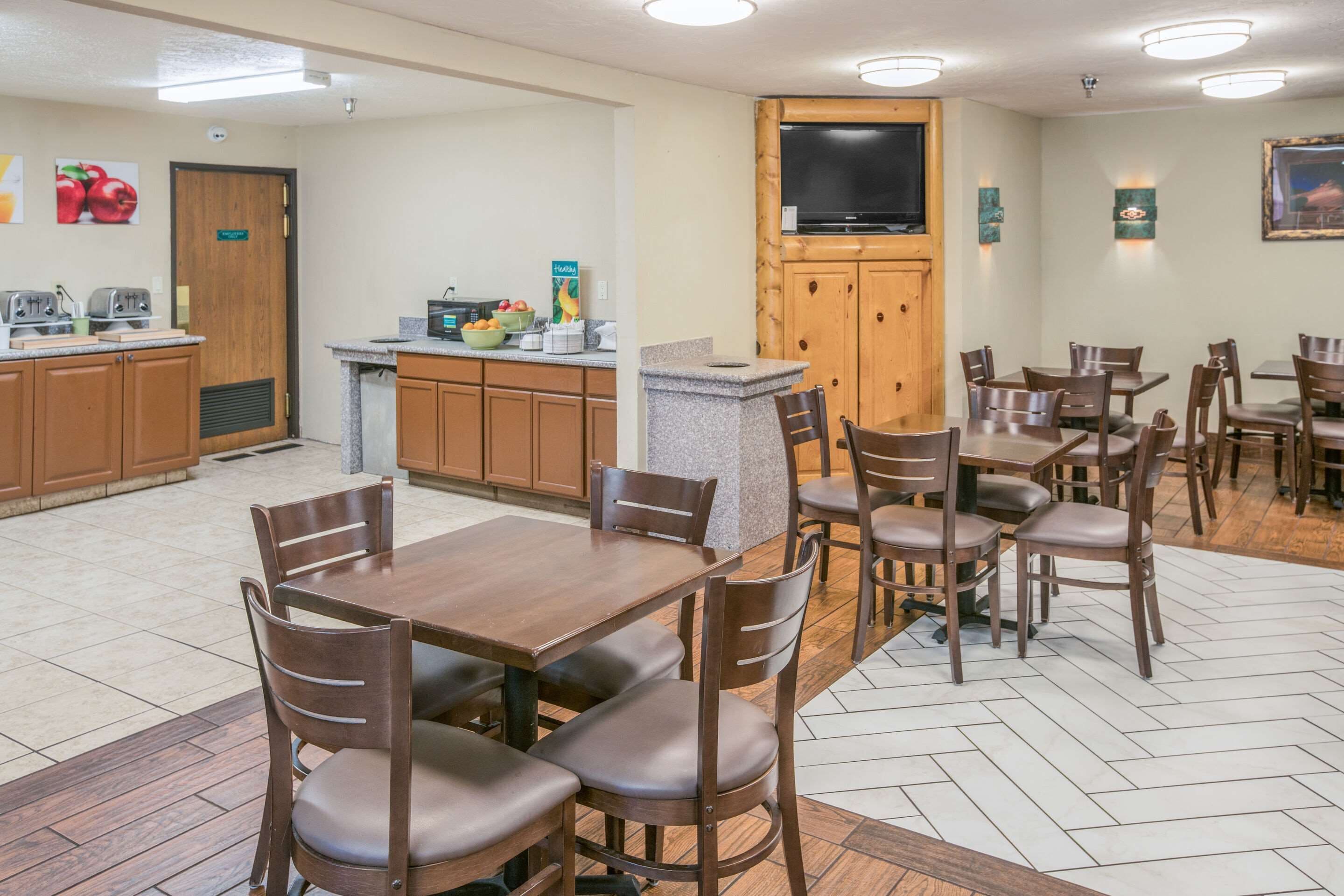 A hotel kitchen with wooden cabinets, a granite countertop, and a television mounted above the cabinets.