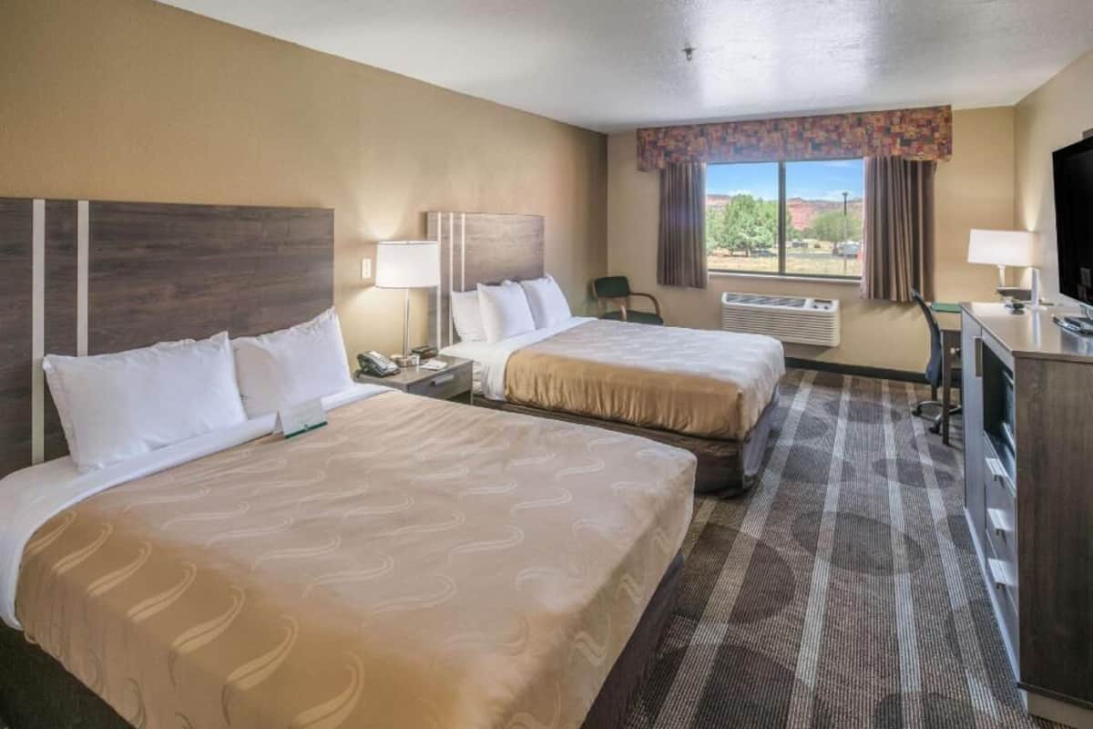 A hotel room with two beds, a desk, a chair, a TV, and a window with a view.