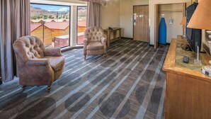 A hotel room with a large window, two armchairs, a wooden desk, a ceiling fan, and a television. - Quality Inn Kanab National Park Area (Kanab)