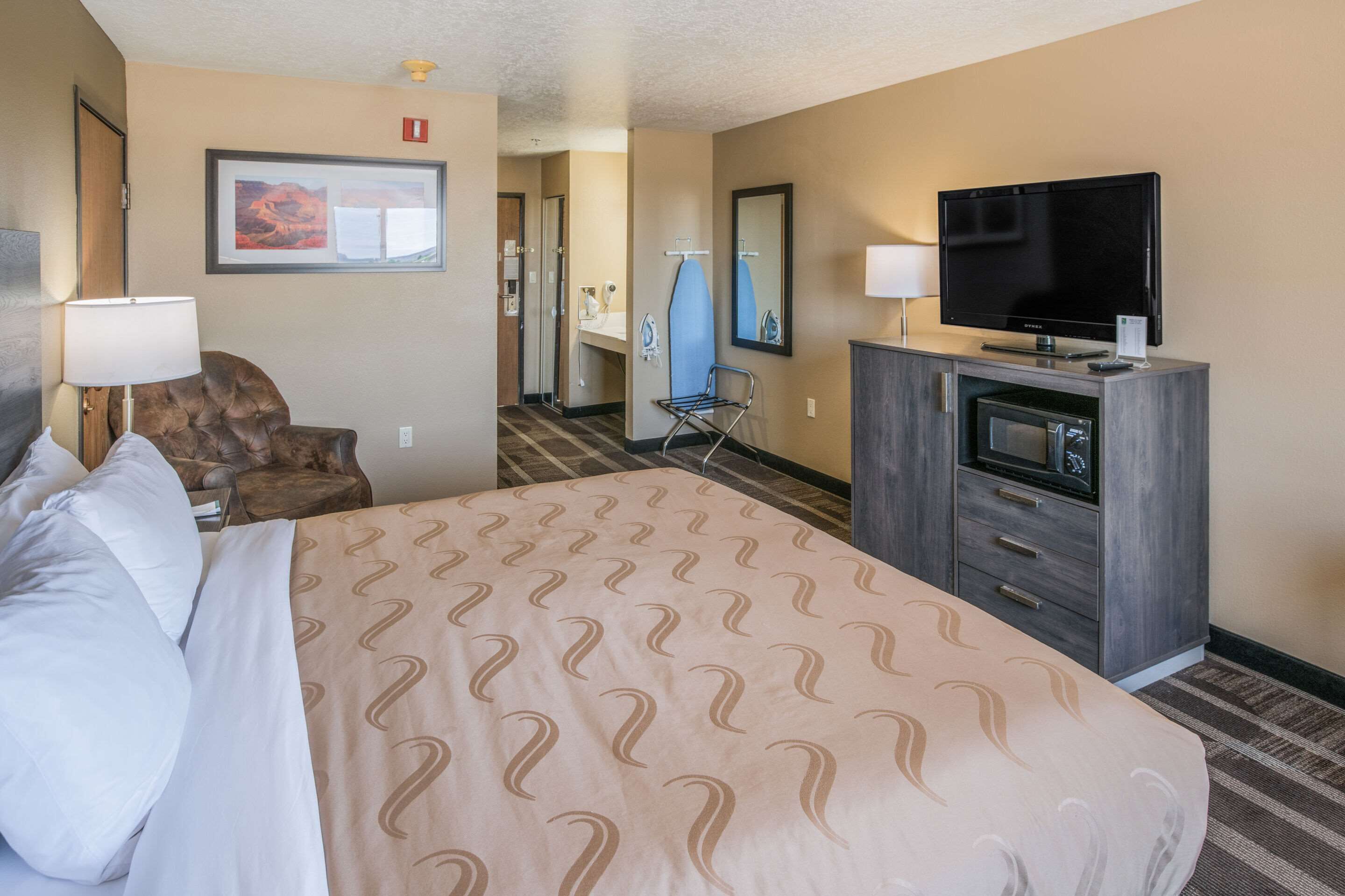 Quarto de hotel com cama grande, televisão, escrivaninha com micro-ondas e uma cadeira.