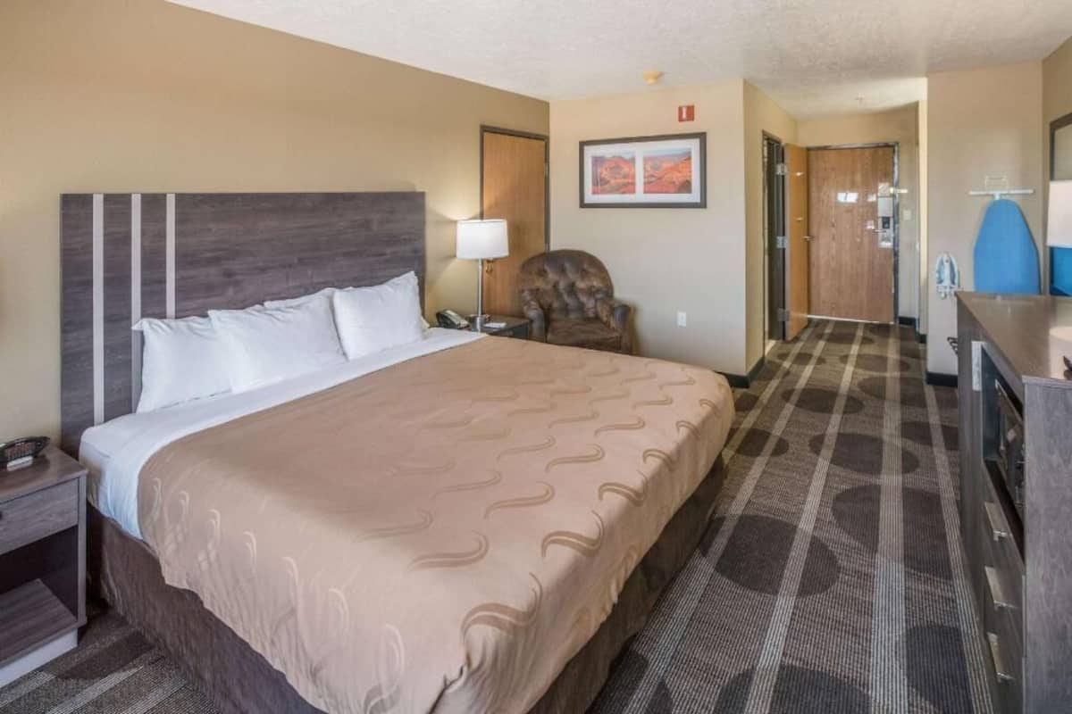 A hotel room with a large bed, a chair, a desk, and a mirror.