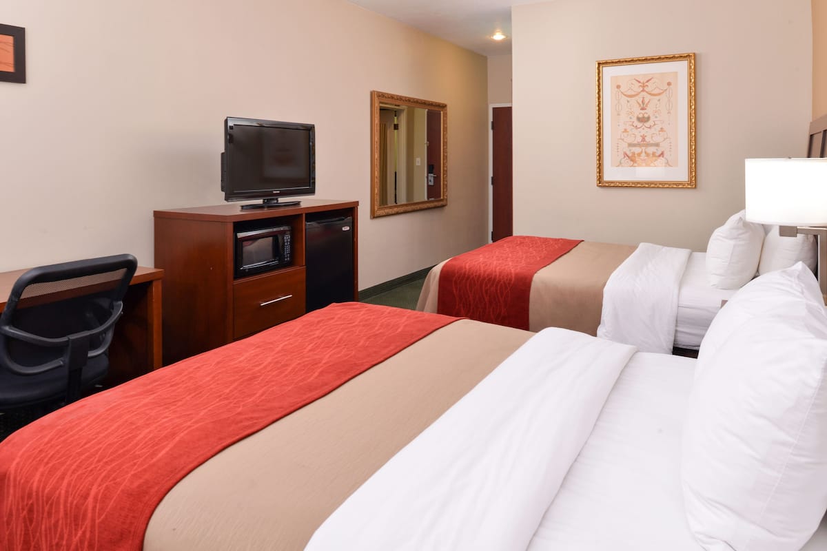 Quarto de hotel com duas camas, uma secretária com televisão, um espelho e um quadro na parede.