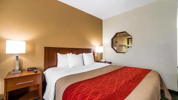 Habitación de hotel con una cama grande, dos lámparas de noche, una mesita de noche con lámpara, un espejo y una colcha roja estampada.