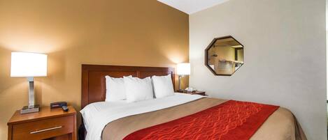 Habitación de hotel con una cama grande, dos lámparas de noche, una mesita de noche con lámpara, un espejo y una colcha roja estampada.