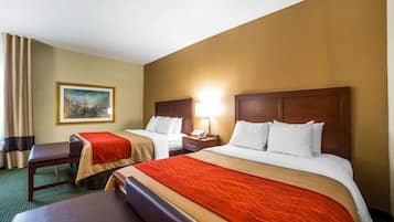 Habitación de hotel con dos camas, un escritorio, una silla, una mesita de noche, una lámpara y un cuadro en la pared.