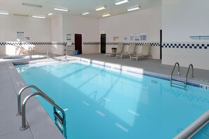 An indoor swimming pool with clear water, a tiled deck, and lounge chairs.