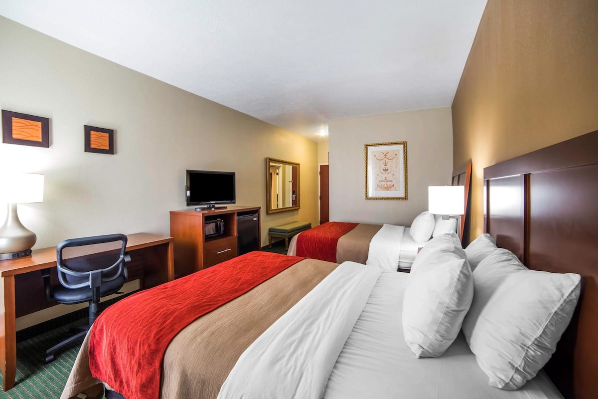 Quarto de hotel com duas camas, uma mesa de trabalho com cadeira, televisão e espelho.