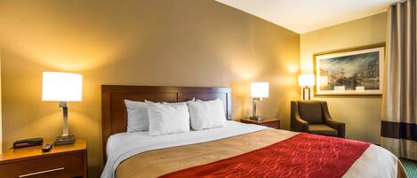 A hotel room with a large bed, two bedside tables with lamps, a chair, and a painting on the wall.
