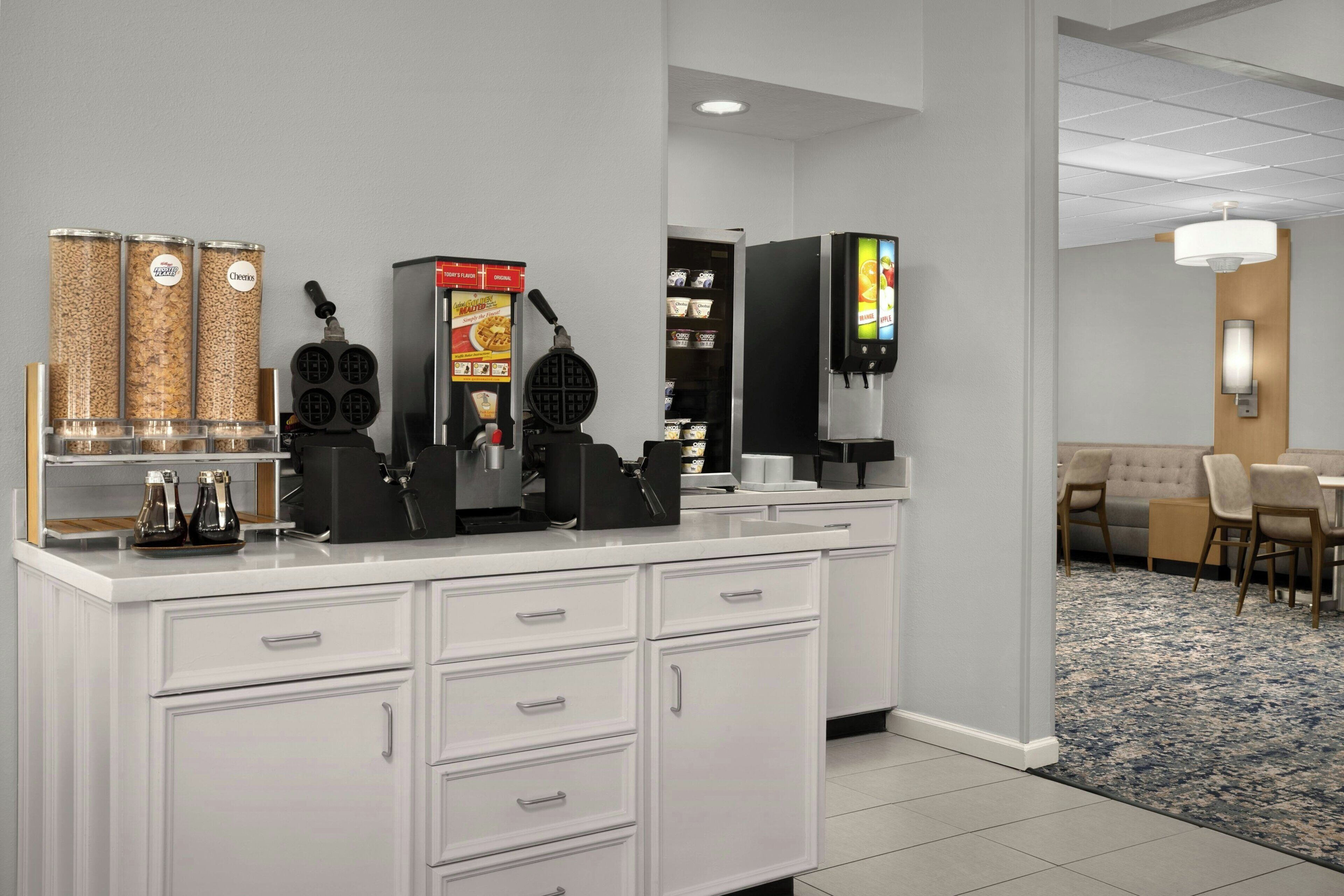 A modern hotel room with a kitchenette, a dining area, and a living space.