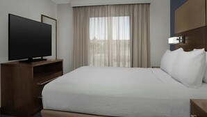 A hotel room with a bed, a TV on a wooden stand, a window with curtains, and a headboard with a light fixture. - Residence Inn by Marriott Provo North University (Provo)