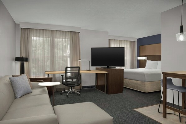 A hotel room with a sofa, a bed, a desk with a TV, a chair, and a lamp.