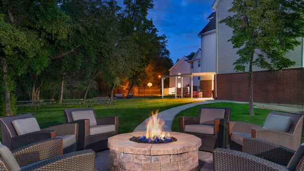 A backyard with a stone fire pit surrounded by wicker furniture, a lawn, and a house in the background. - Residence Inn by Marriott Provo North University (Provo)