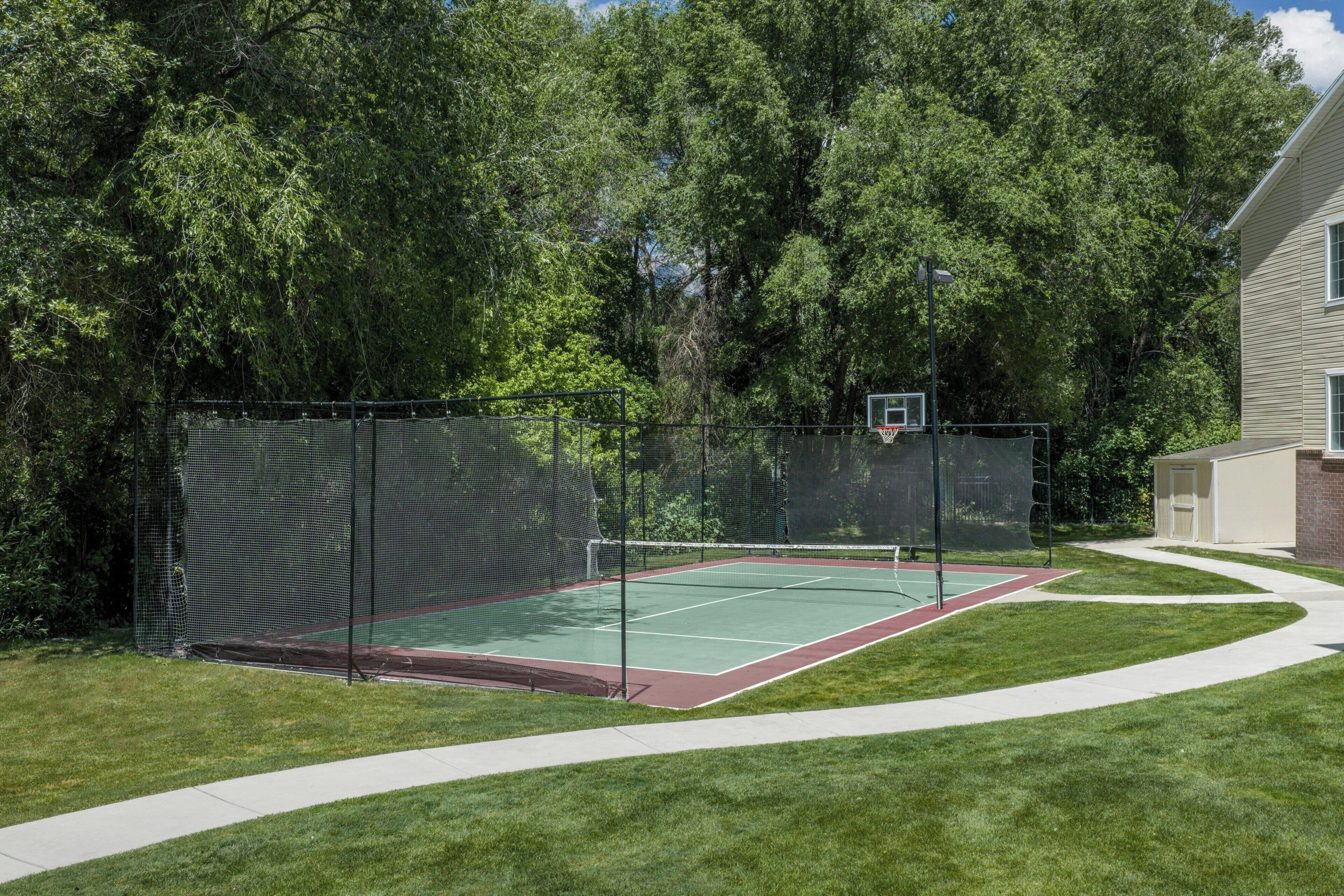 Een tennisbaan met een net, omringd door een hek en bomen.