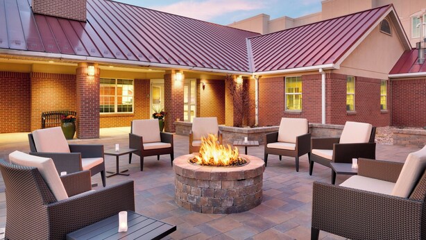An outdoor patio area with a stone fire pit surrounded by wicker furniture and a brick wall.