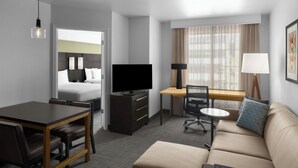 A hotel room with a bed, a desk, a sofa, a TV, and a dining area.