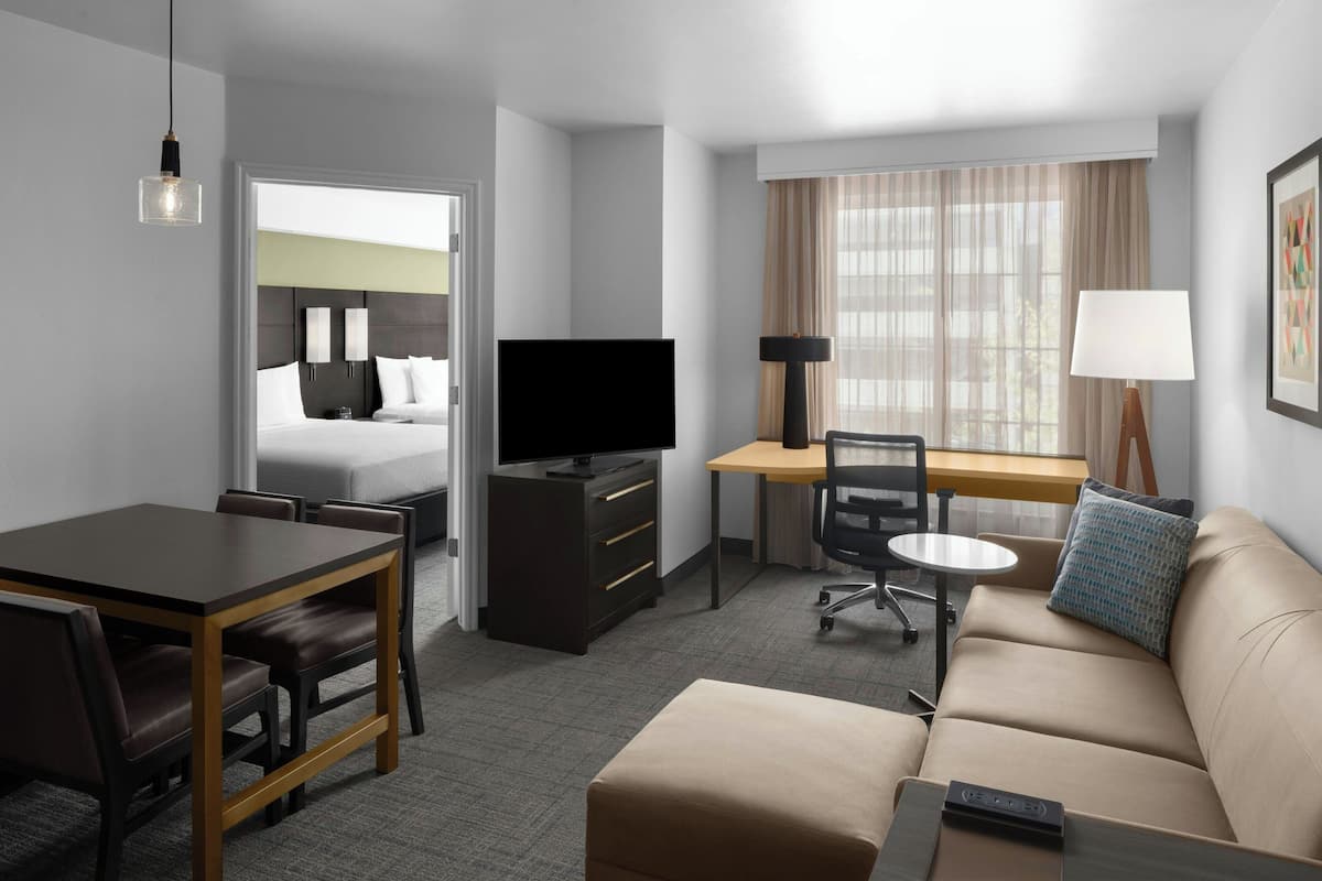 Habitación de hotel con cama, escritorio, sofá, televisor y zona de comedor.
