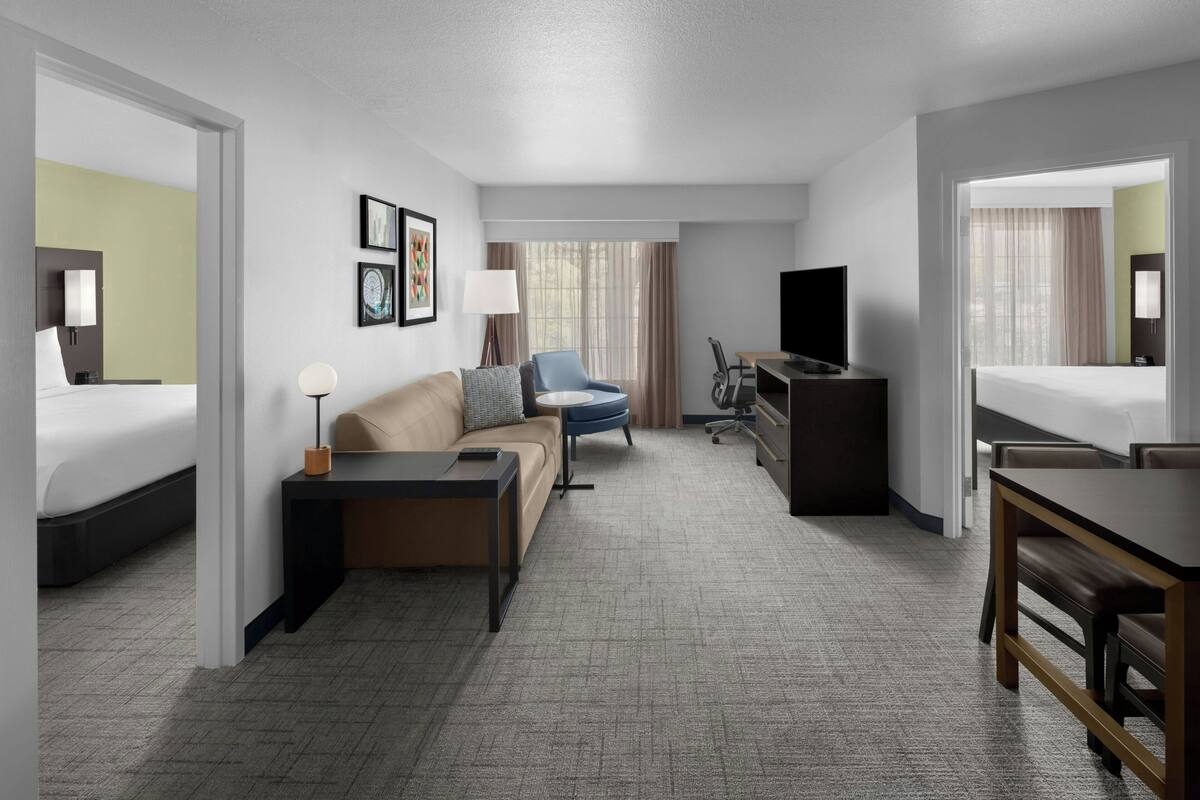 Habitación de hotel con cama, sofá, escritorio, silla, televisión y ventana con cortinas.